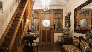 A wooden staircase leading to a room with a chandelier, a door with a decorative glass panel, a wooden cabinet, and a striped sofa. - 79 On Ridge BNB (Pietermaritzburg)