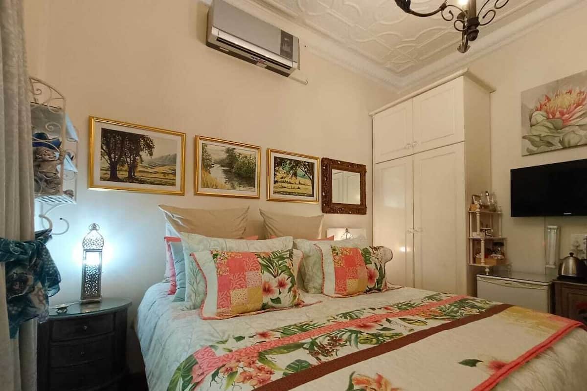 A bedroom with a floral bedspread, a nightstand with a lamp, and a wall-mounted TV.