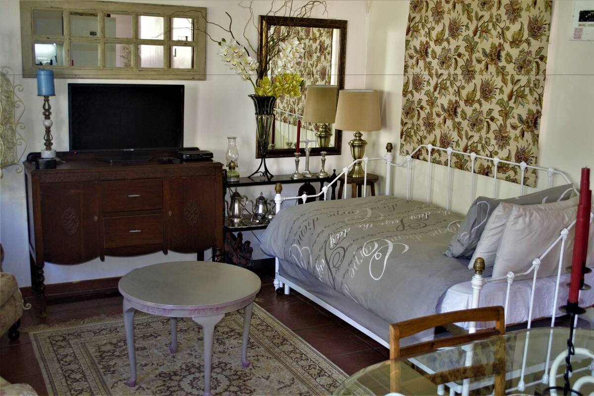A bedroom with a bed, bedside table, dresser, TV, and decorative items.