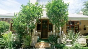 A house with a central entrance, surrounded by lush greenery and a small garden. - 79 On Ridge BNB (Pietermaritzburg)