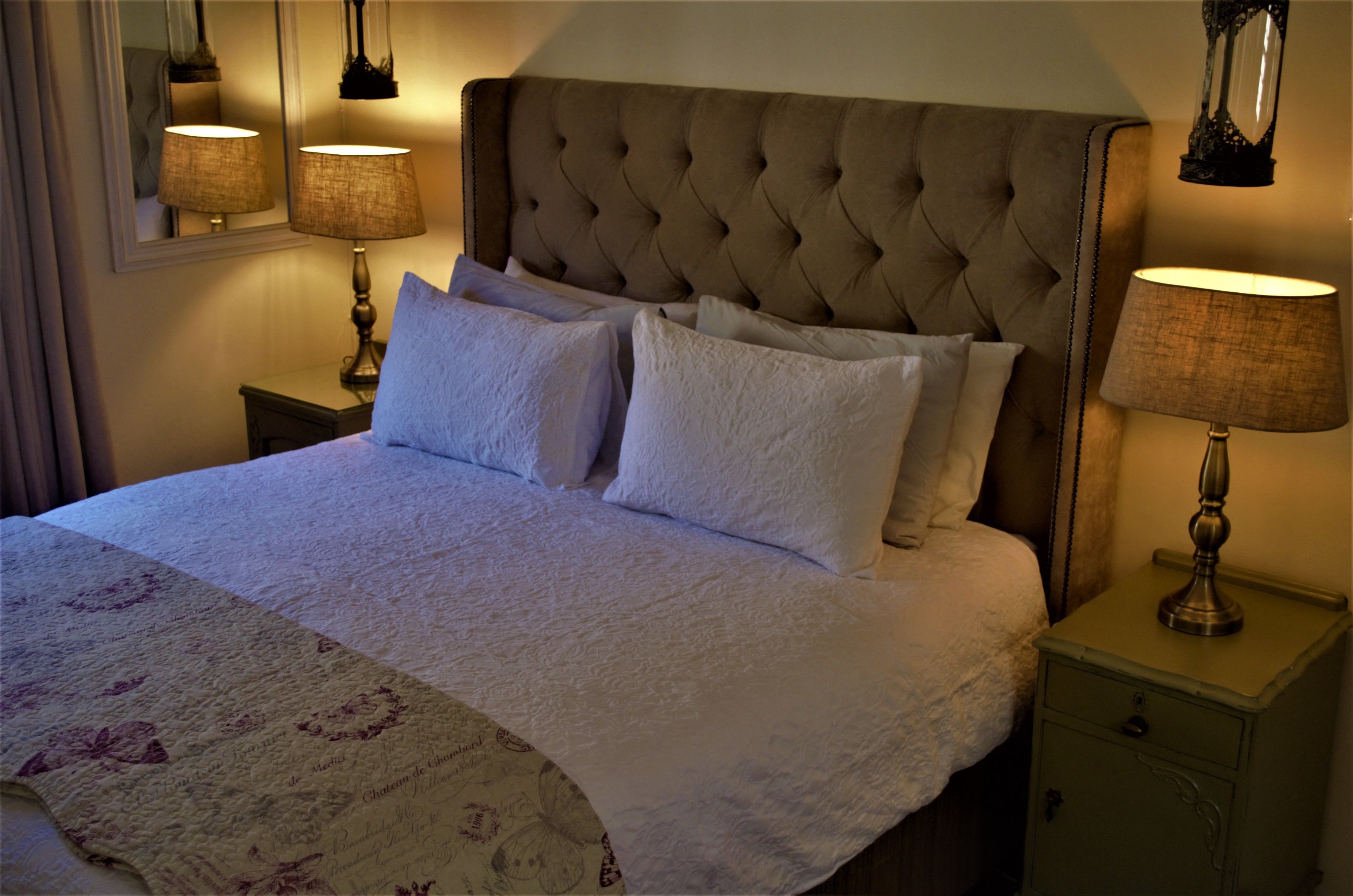 A neatly made bed with a tufted headboard, two bedside tables with lamps, and a mirror on the wall.