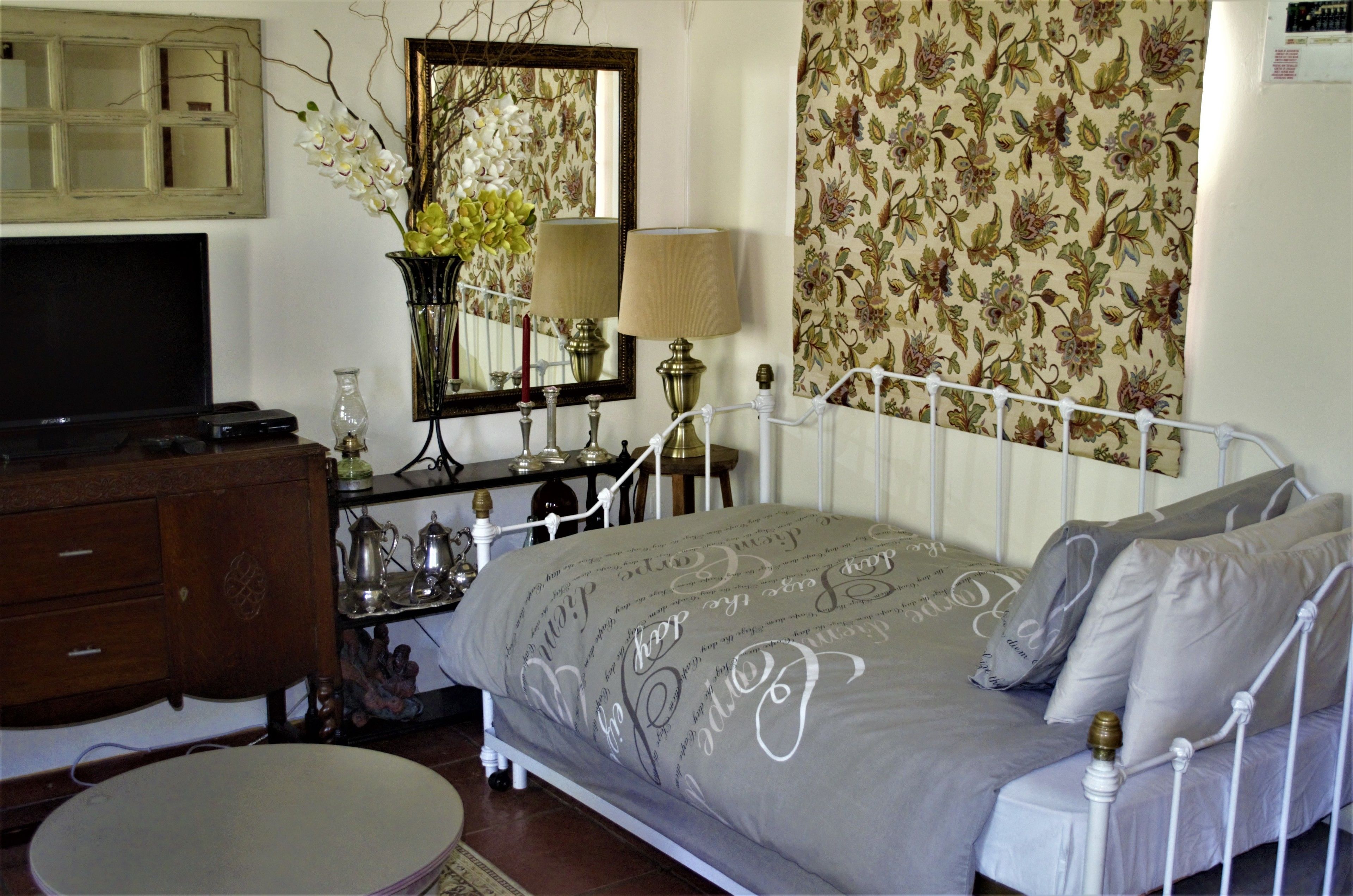 Une chambre à coucher avec un lit, une commode, une télévision, un miroir et un papier peint à motifs floraux.