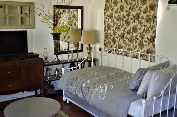 A bedroom with a bed, a dresser, a TV, a mirror, and a floral wallpaper.