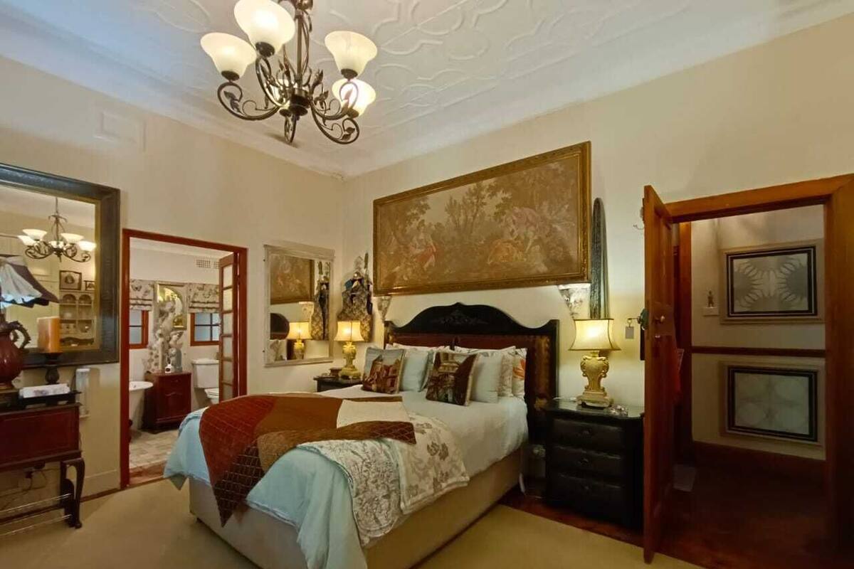 A spacious bedroom with a large bed, a chandelier, and a painting above the bed.
