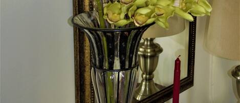 A vase with white and yellow orchids, a mirror, and a red candle on a table.