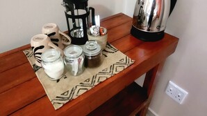 A wooden table with a coffee maker, a kettle, and various containers on a patterned cloth. - Mondjila Safari Camp - Campsite (Outjo)