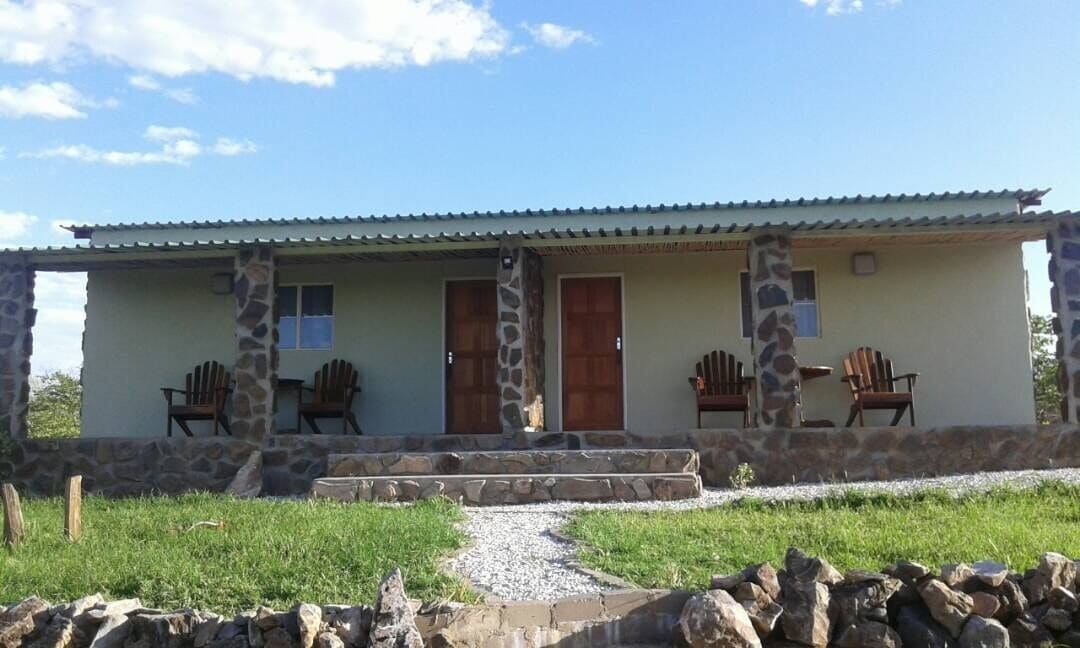 Un edificio de piedra de dos pisos con techo plano, dos puertas de madera y un porche cubierto con cuatro sillas Adirondack.