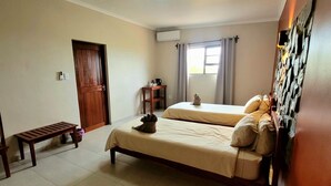 A room with two beds, a bench, a small table, and a window with curtains. - Mondjila Safari Camp - Campsite (Outjo)