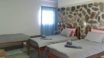 Une chambre avec deux lits simples, un mur en pierre, une fenêtre avec des rideaux et un banc en bois.