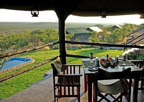 An outdoor dining area with a view of a pool and landscape. - Mondjila Safari Camp - Campsite (Outjo)