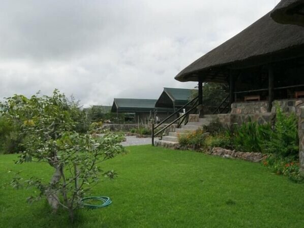 A house with a thatched roof, stone steps, and a well-maintained lawn. - Mondjila Safari Camp - Campsite (Outjo)