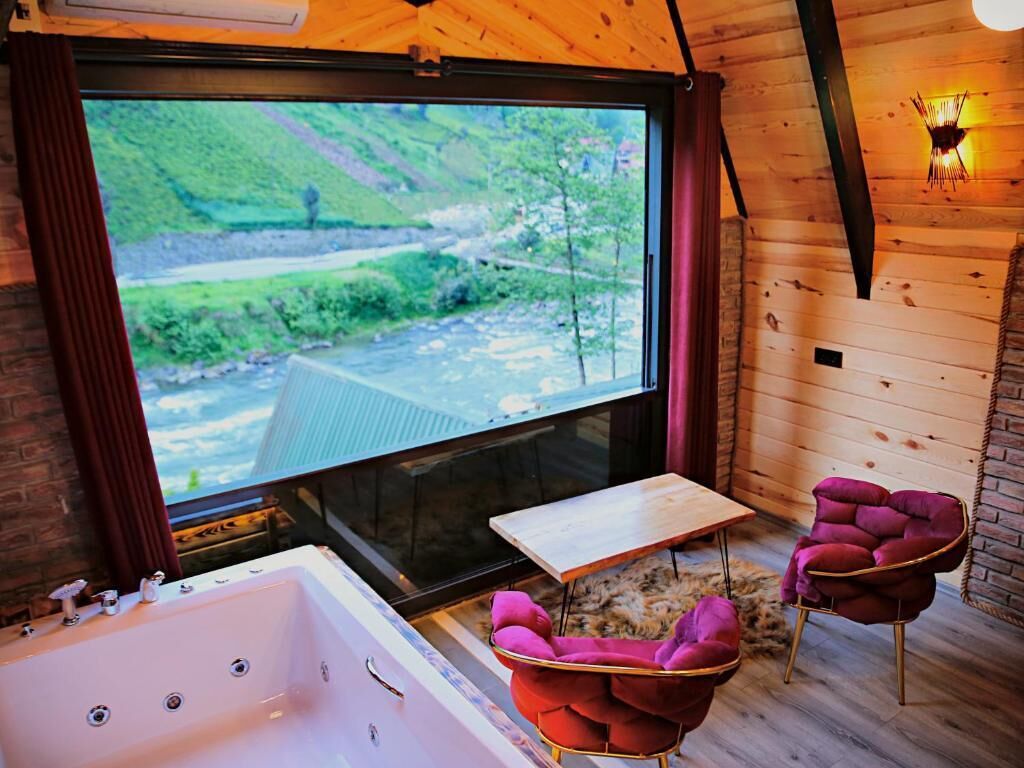 Une pièce avec une grande fenêtre, une baignoire et deux fauteuils roses.