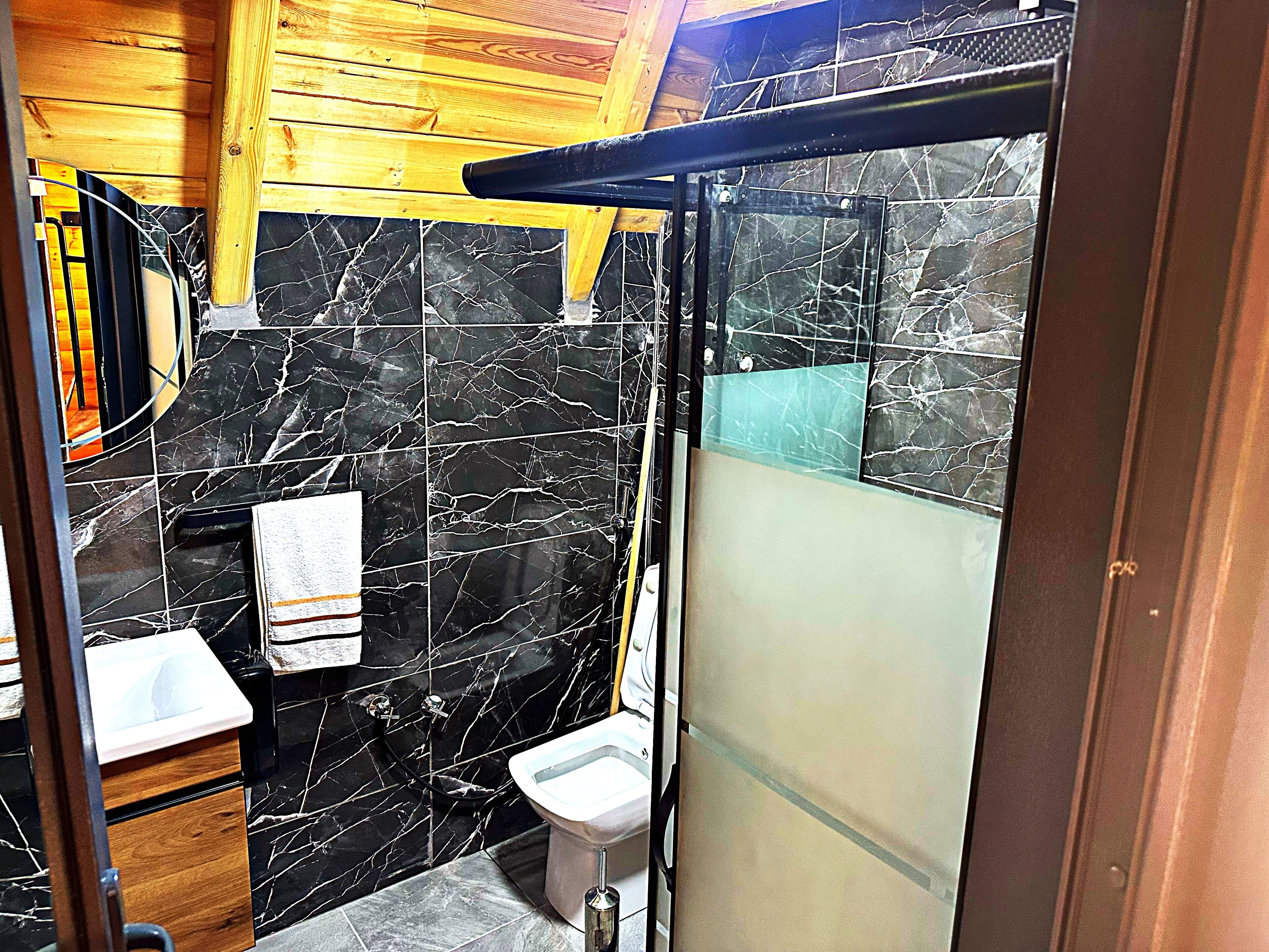 A bathroom with black marble tiles, a wooden ceiling, a white sink, and a toilet.