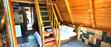 Un intérieur en bois avec un lit en mezzanine, un escalier en bois et un sol carrelé en pierre.