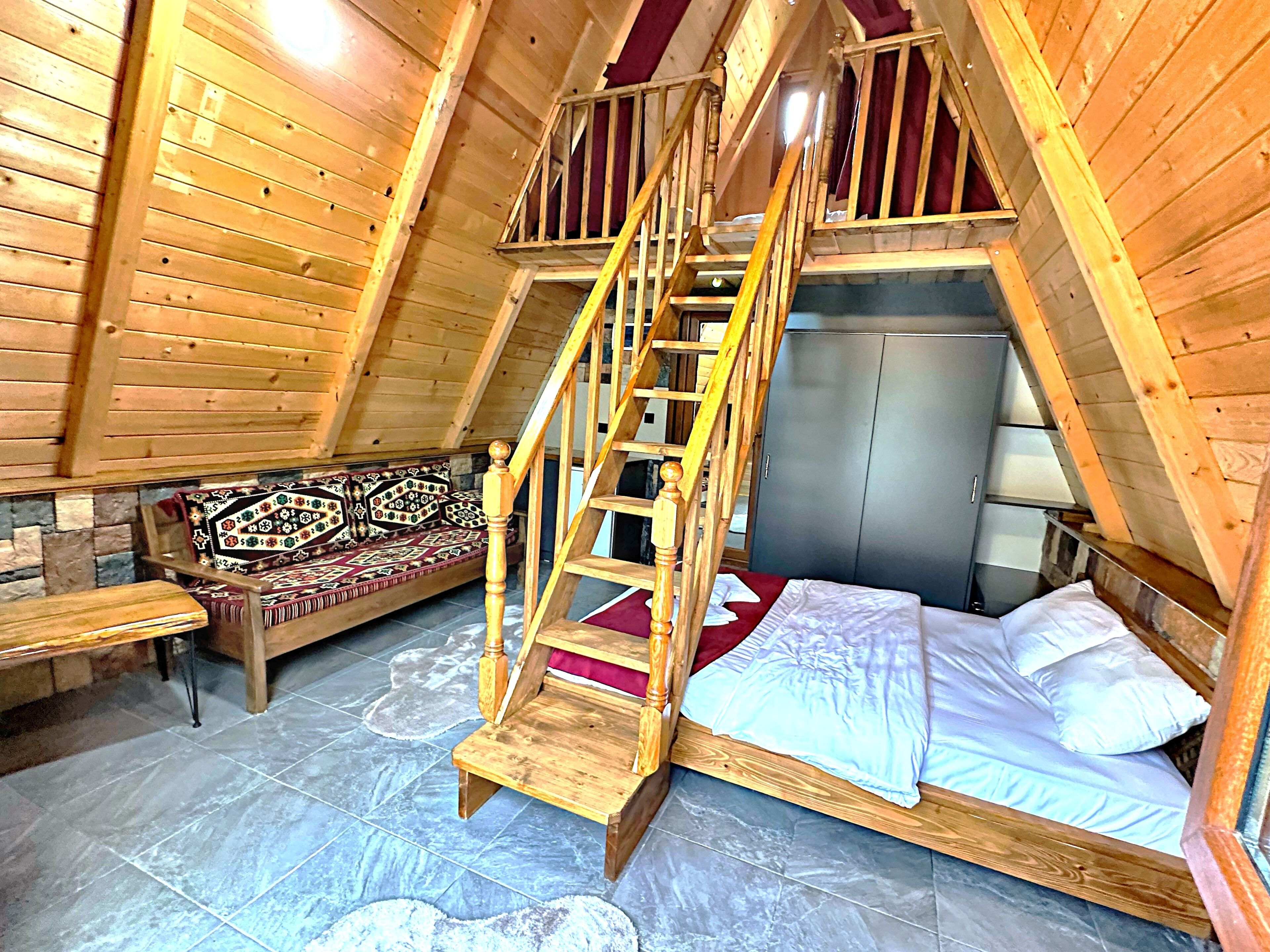A cozy attic bedroom with a wooden staircase, a bed, a bench, and a wardrobe.