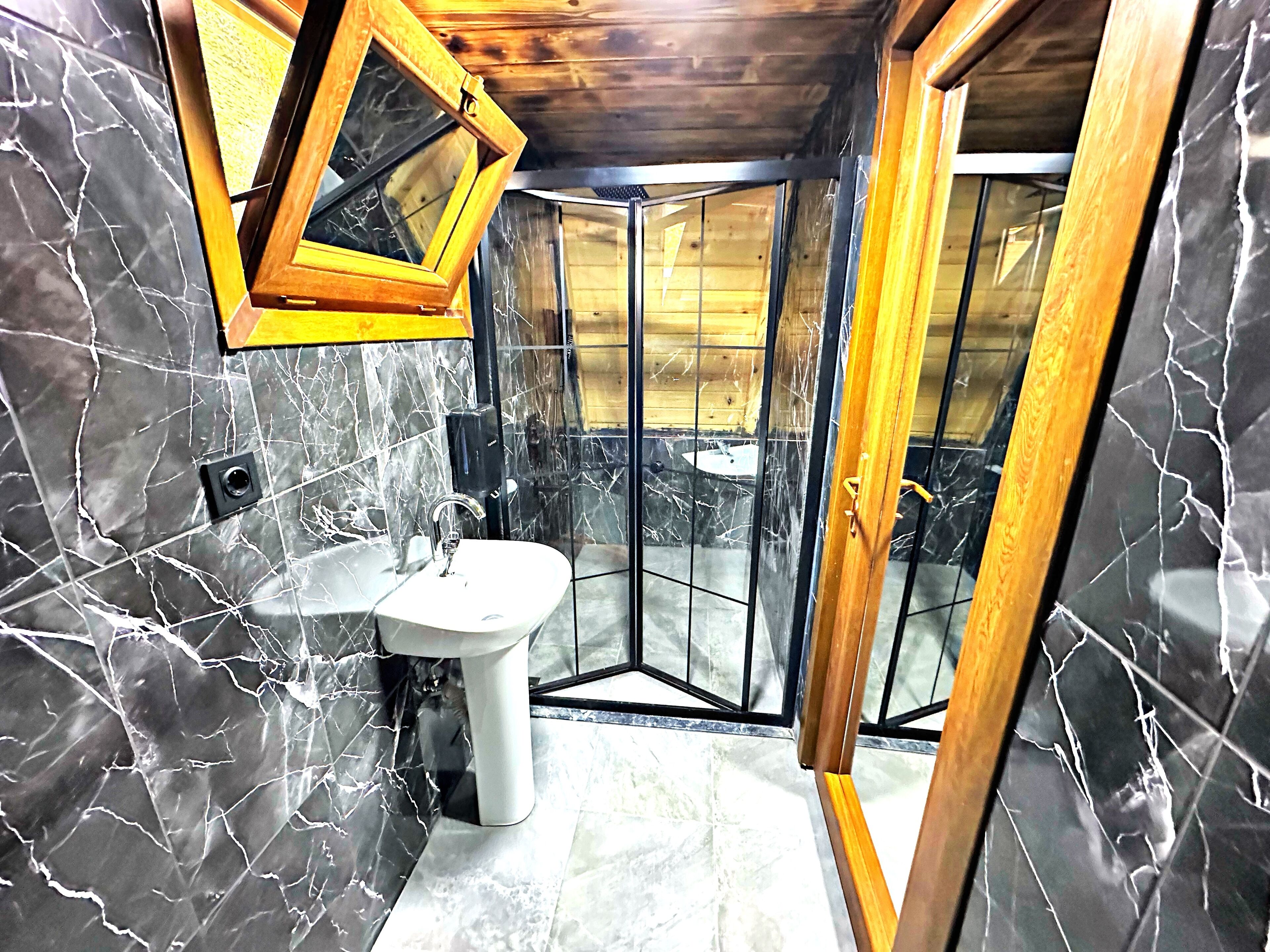 Un baño con lavamanos de mármol, techo de madera y zona de ducha con puertas de vidrio.