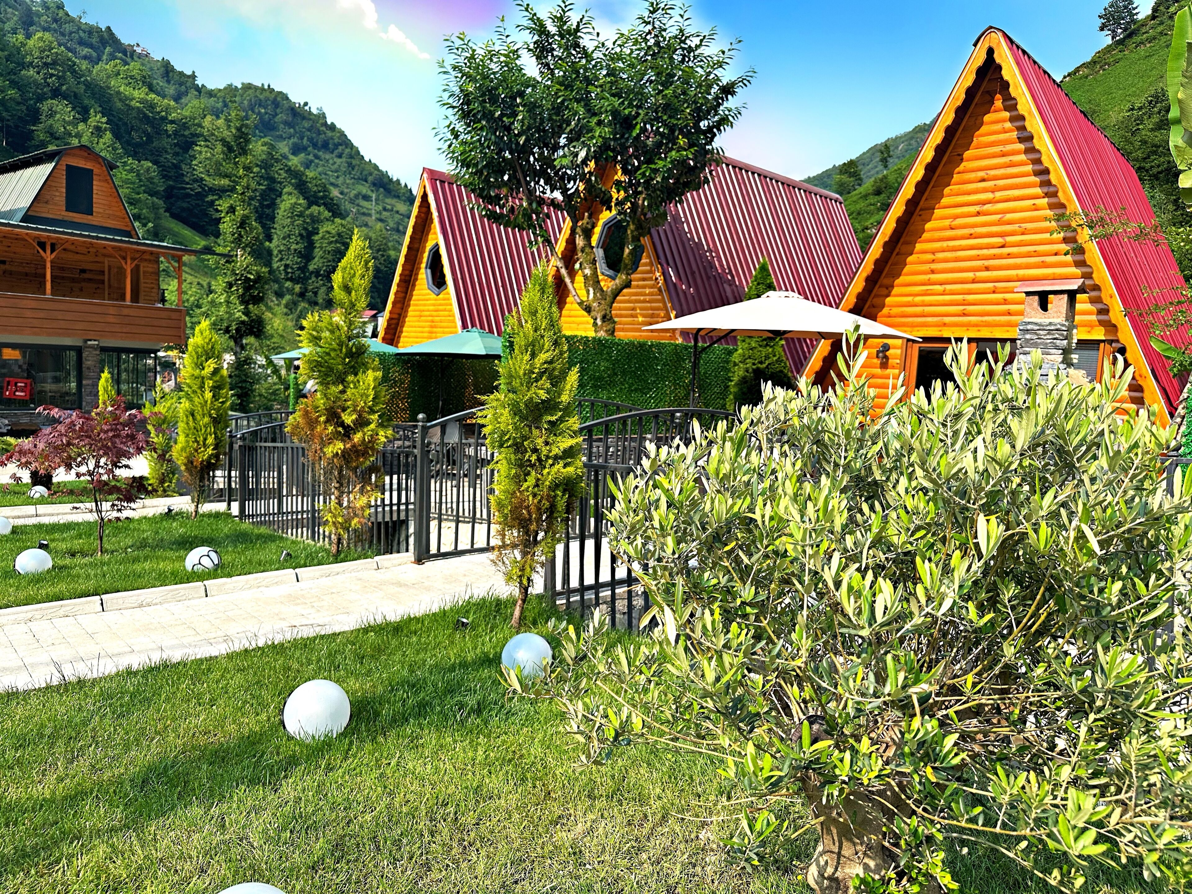 Uma casa de madeira rústica com telhado vermelho, rodeada por vegetação exuberante e céu claro.