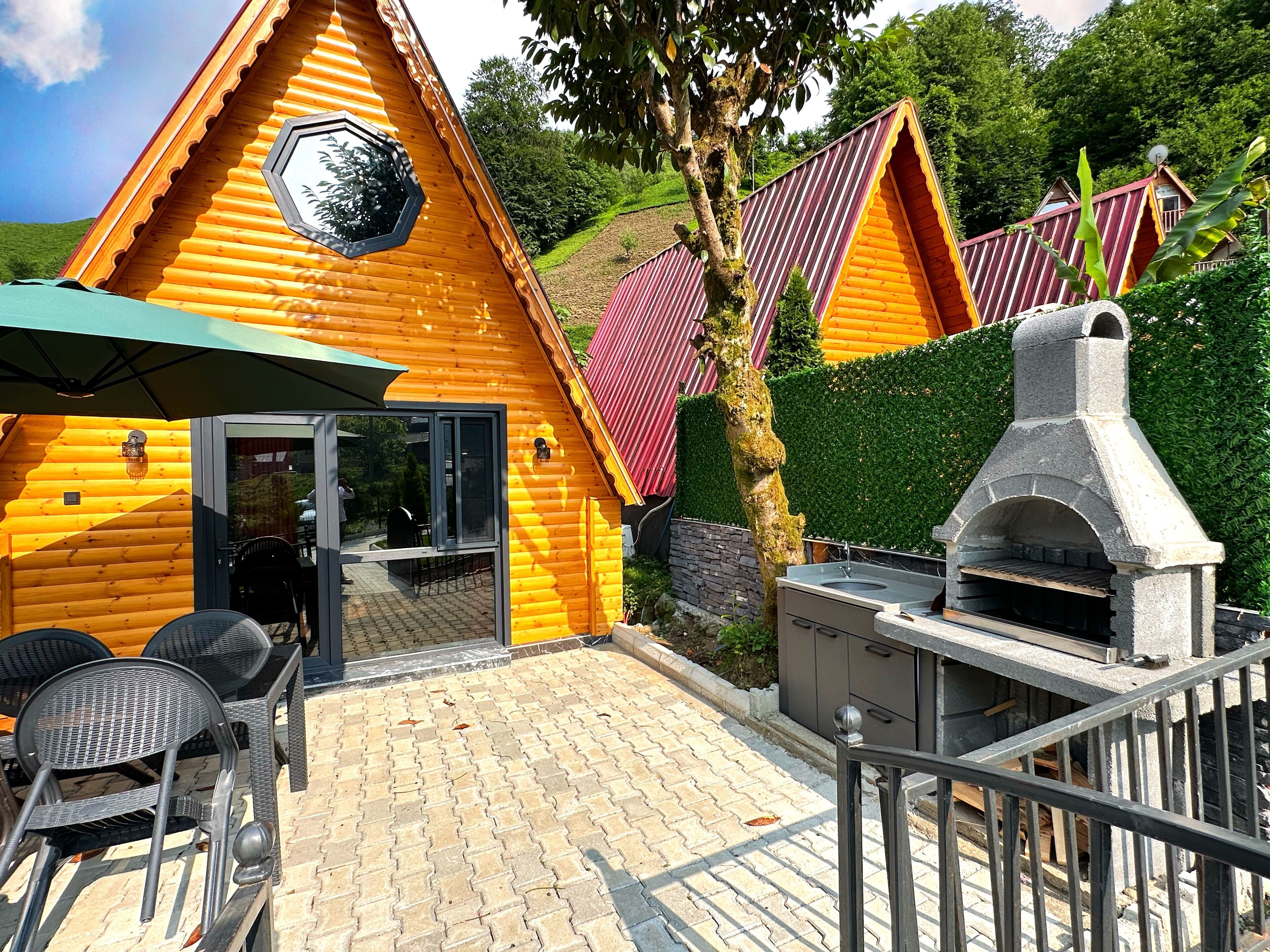 A log cabin with a stone oven, outdoor seating, and a view of the surrounding greenery.