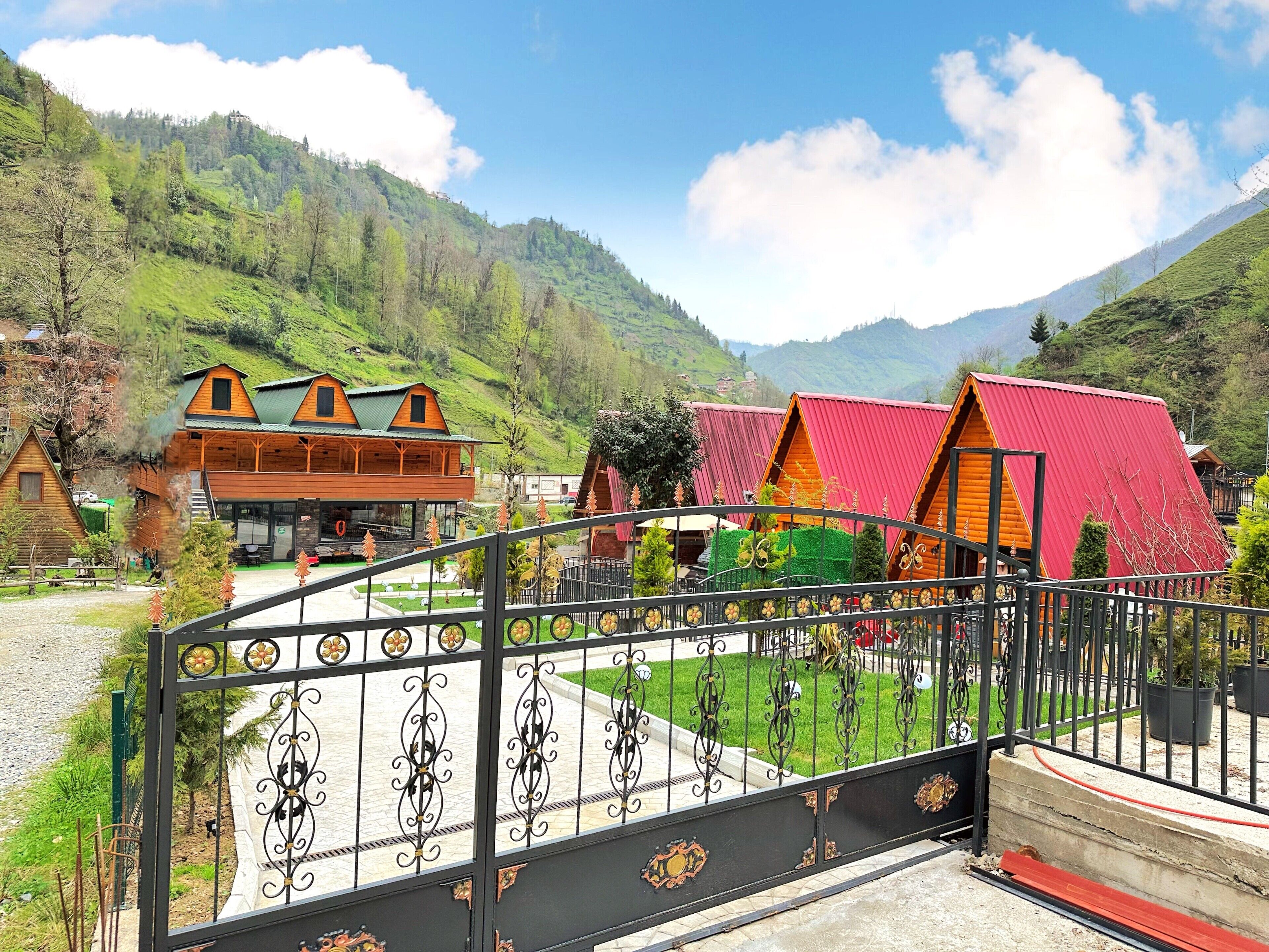 A mountain lodge with wooden cabins and a red-roofed structure, surrounded by lush greenery and hills.