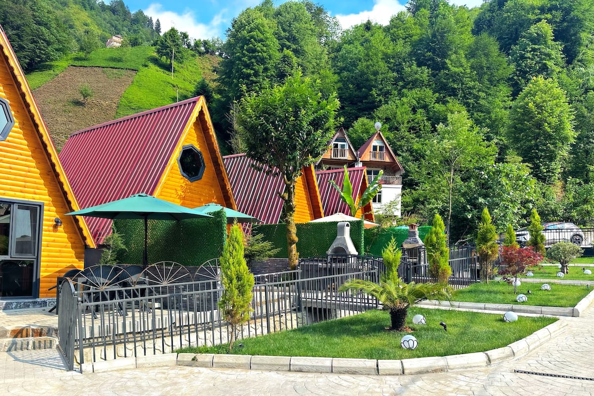 A row of colorful wooden houses with a paved walkway and a fenced garden area.