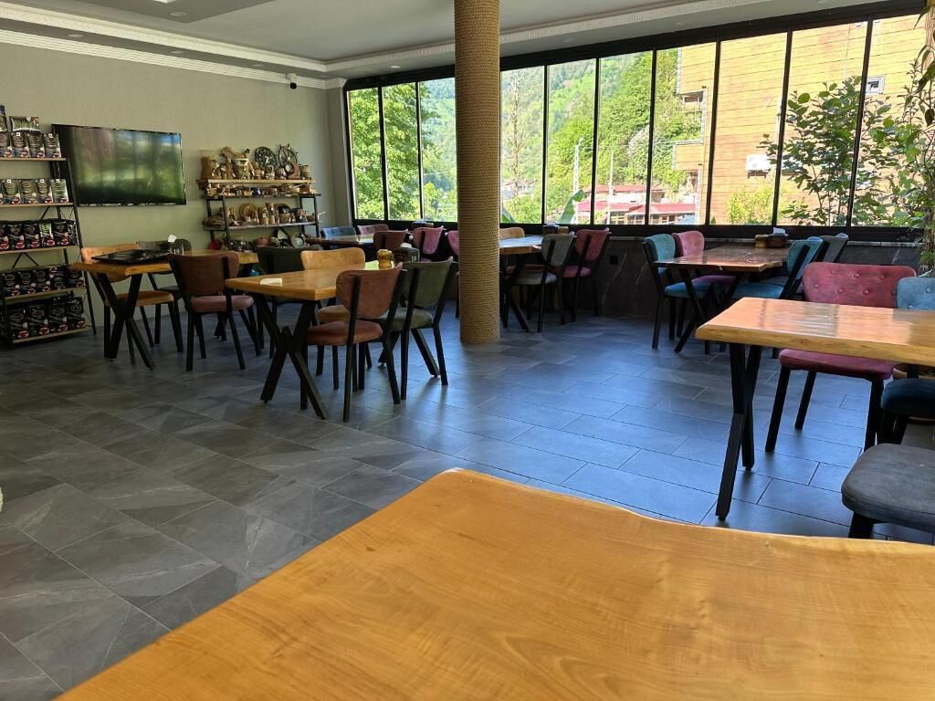 Un restaurante con mesas y sillas de madera, un pilar grande y vistas a árboles a través de amplios ventanales.