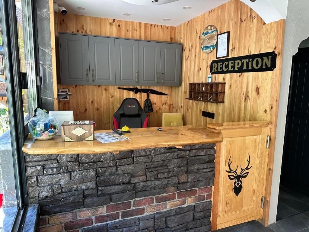 Un área de recepción con mostrador de madera, base de piedra, armarios grises, un letrero de recepción y una decoración con cabeza de ciervo.