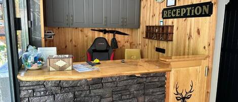 Un área de recepción con mostrador de madera, base de piedra, armarios grises, un letrero de recepción y una decoración con cabeza de ciervo.