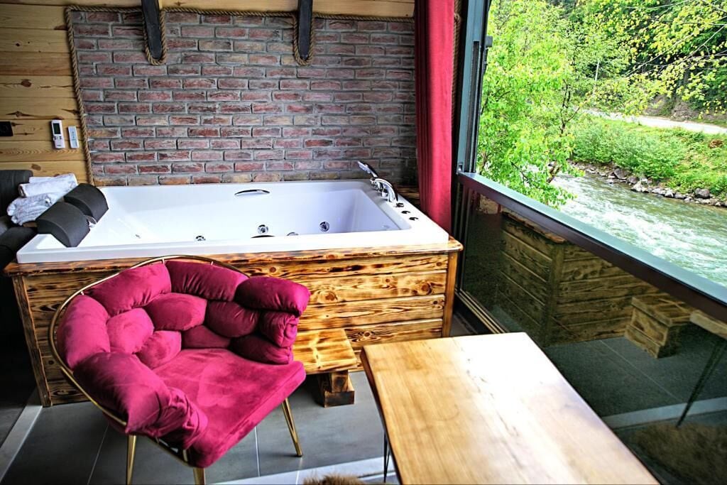 Ein modernes Badezimmer mit einer großen Badewanne, einem Holzbadezimmer-Möbel und Blick auf einen Fluss.
