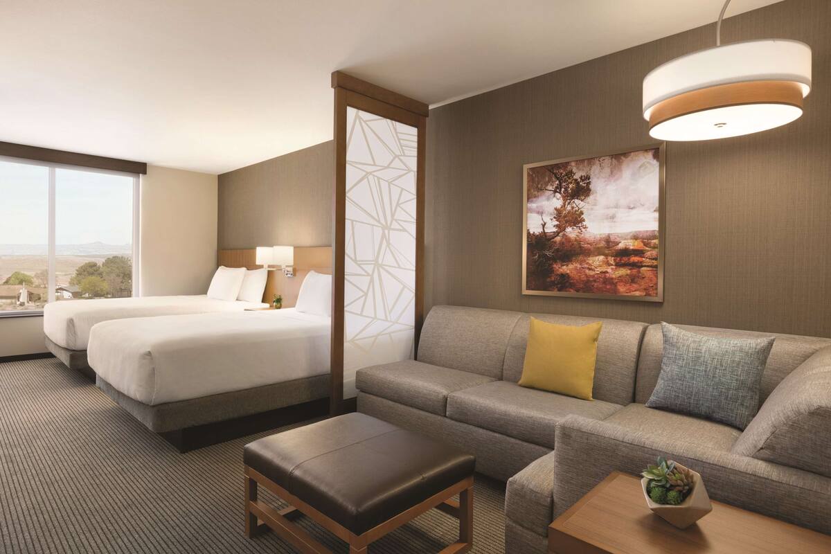 A hotel room with two beds, a sofa, a coffee table, and a large window offering a view.