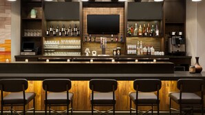 A bar area with a long counter, multiple shelves with bottles, glasses, and a flat-screen TV. There are bar stools and a coffee machine. - Hyatt Place Page Lake Powell (Page)
