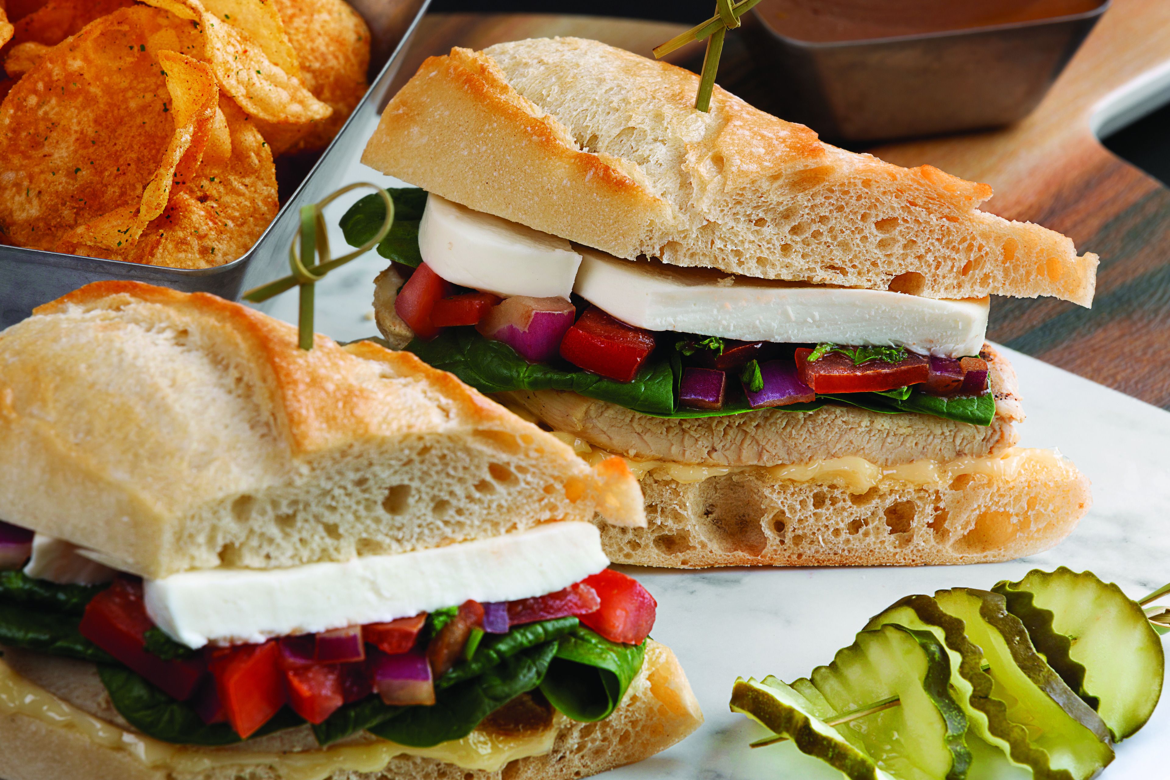 A sandwich with various ingredients and a side of chips.