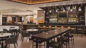 A modern bar area with multiple seating options, including bar stools and round tables, and a television mounted on the wall. - Hyatt Place Page Lake Powell (Page)