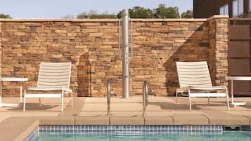 A pool area with two lounge chairs and a stone wall.