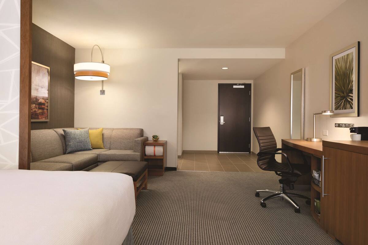 A hotel room with a bed, a sofa, a desk, and a chair. There is a door leading to another room.