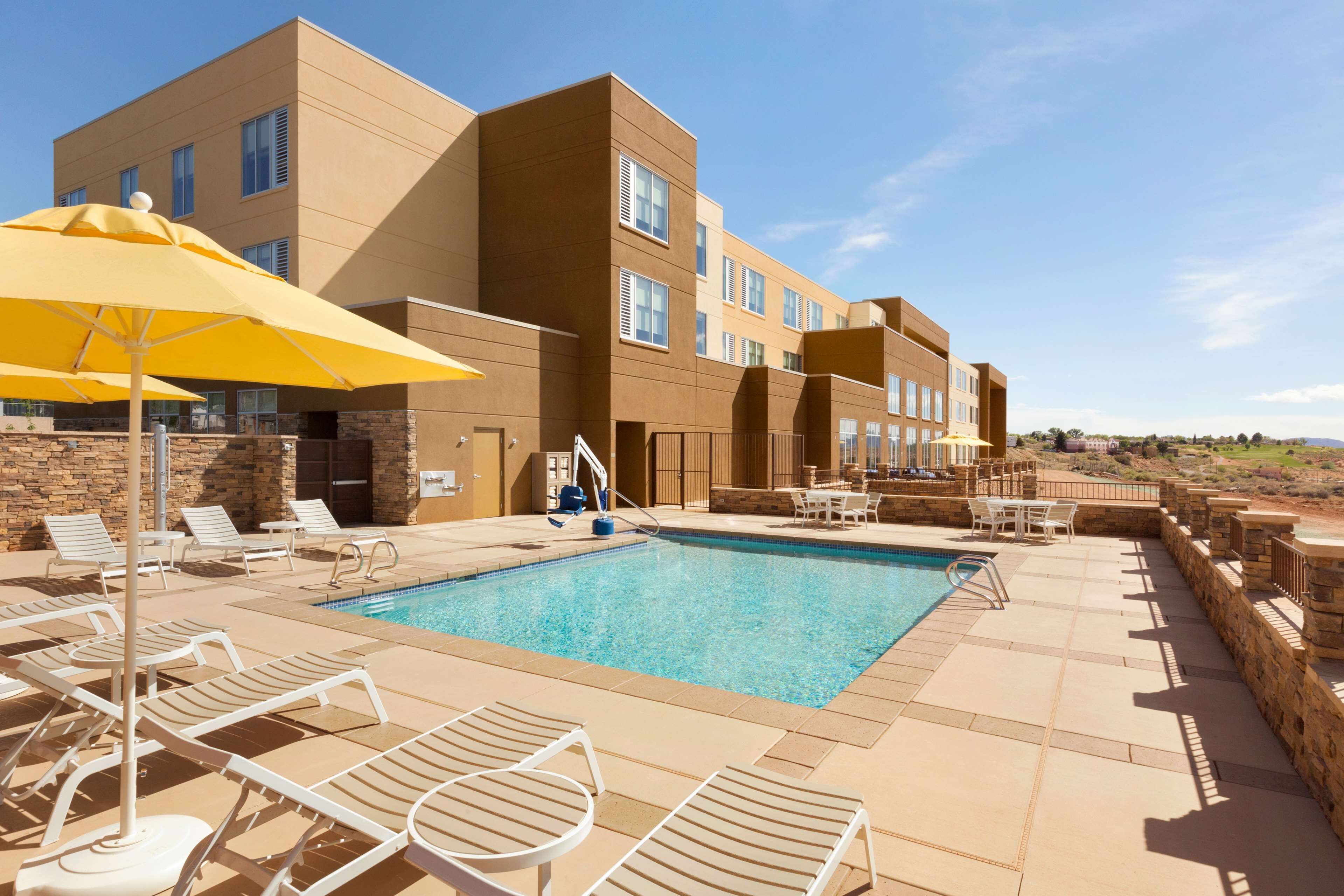 A pool area with lounge chairs and umbrellas, a clear blue pool, and a modern building with multiple windows.