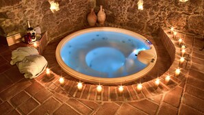 A stone-walled room with a circular hot tub, candles, and a bottle of champagne. - Solar Antigo Luxury Spa Coimbra (Coimbra)