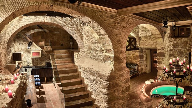 A stone-walled interior with a wooden staircase, a pool area with candles, and a chandelier. - Solar Antigo Luxury Spa Coimbra (Coimbra)