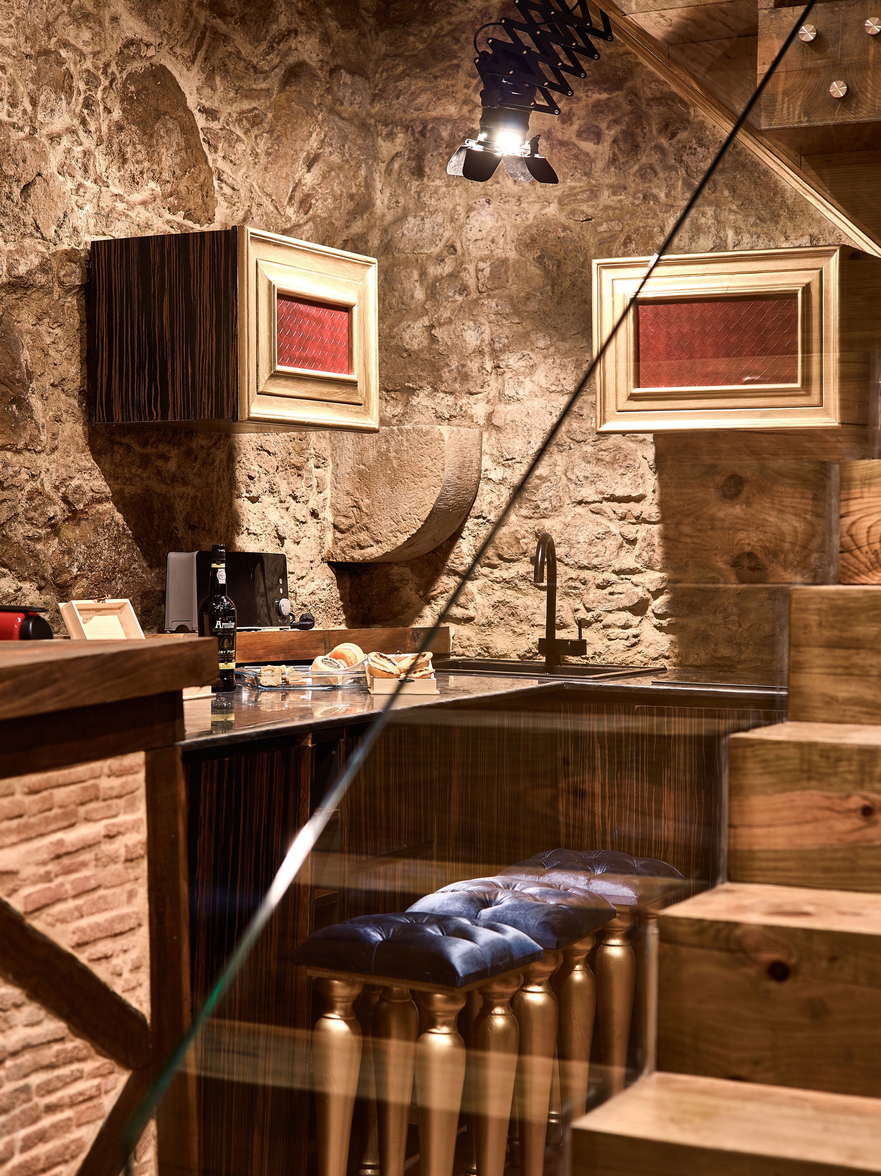 A rustic bar area with wooden stools, a stone wall, and framed pictures on the wall.