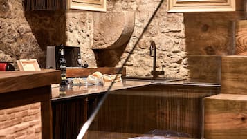 A rustic bar area with wooden stools, a stone wall, and framed pictures on the wall.