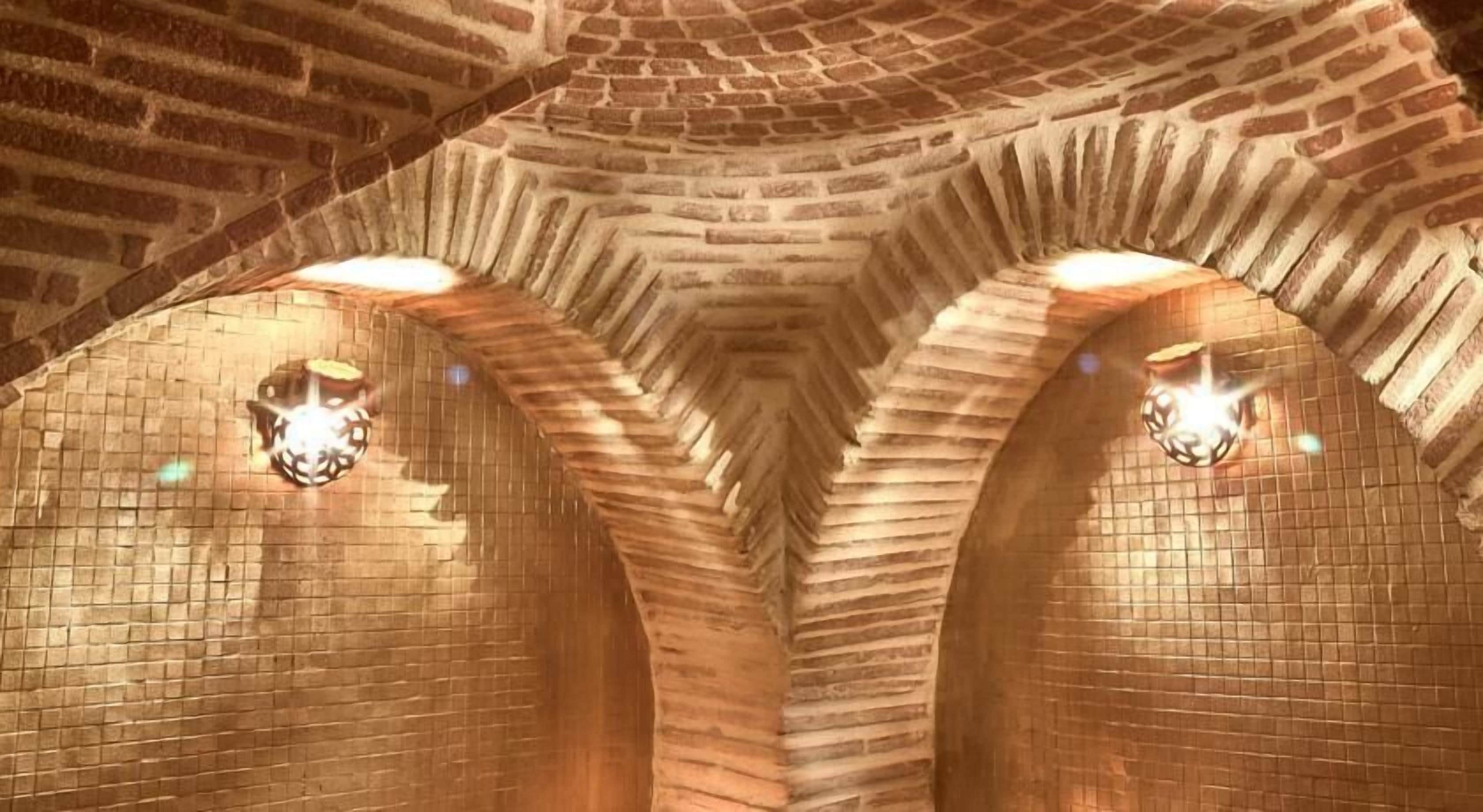 A vaulted brick ceiling with arched niches and wall-mounted light fixtures.