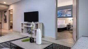 Une chambre d’hôtel moderne équipée d’un téléviseur à écran plat, d’un vase blanc orné de fleurs, d’une console et d’un lit avec une table de chevet.