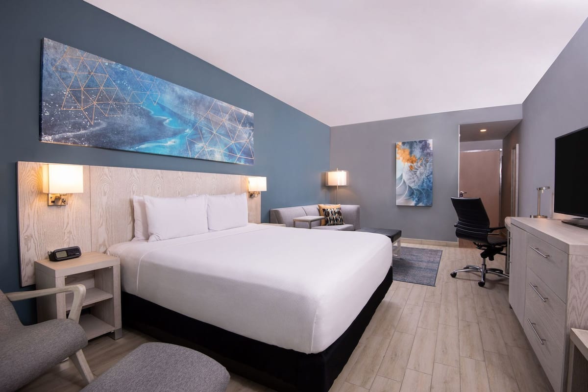 Ein modernes Hotelzimmer mit einem großen Bett, Nachttischen, einem Schreibtisch, einem Sessel und Bildern an den Wänden.
