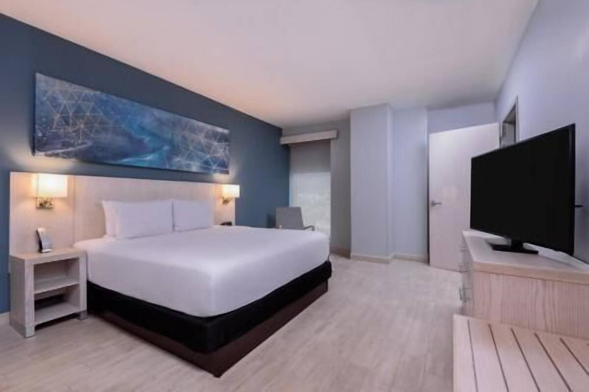 Ein modernes Hotelzimmer mit einem großen Bett, Nachttischen, einem Flachbildfernseher und einem großen abstrakten Gemälde an der Wand.