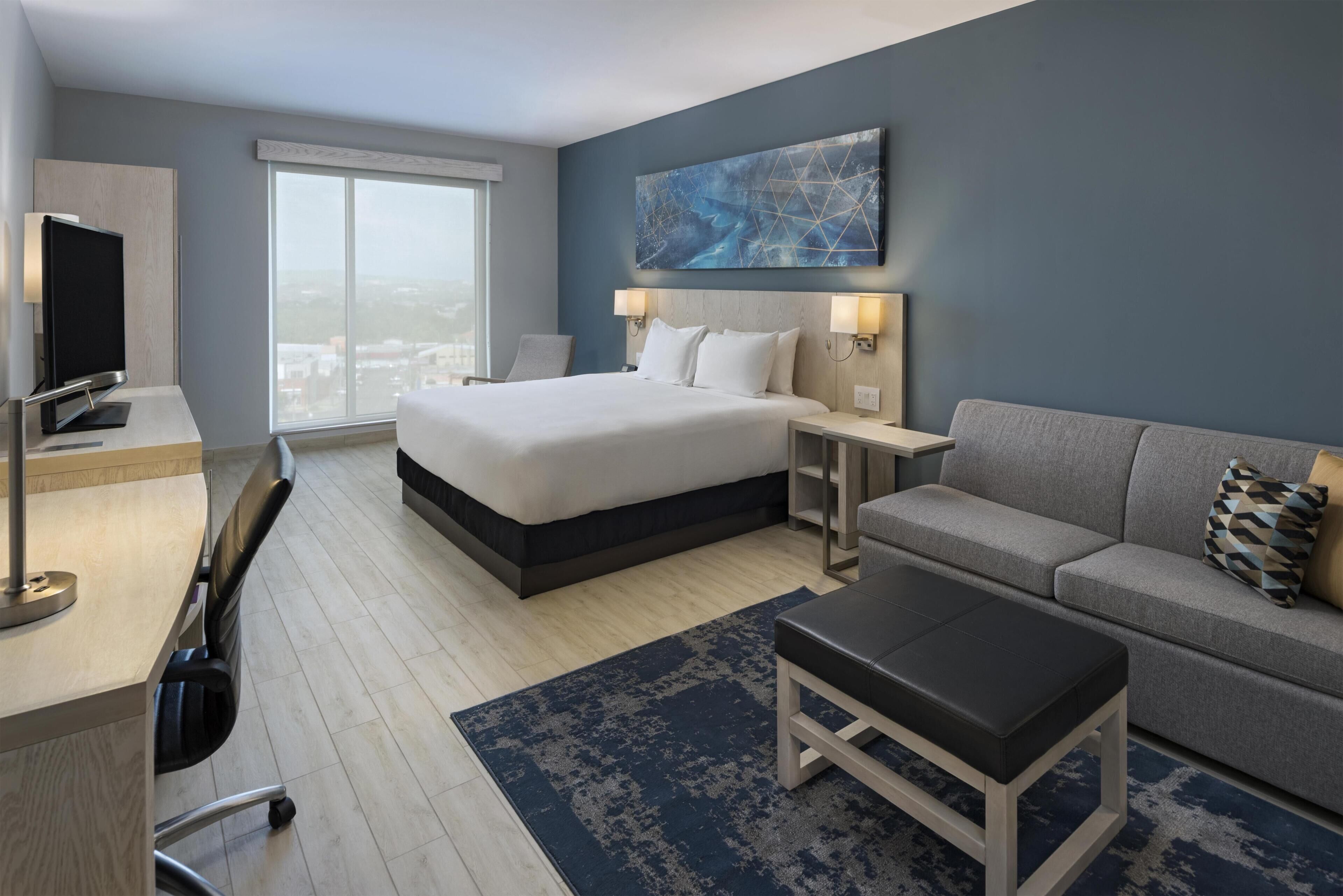 Habitación de hotel con cama, escritorio, sofá y un ventanal grande.