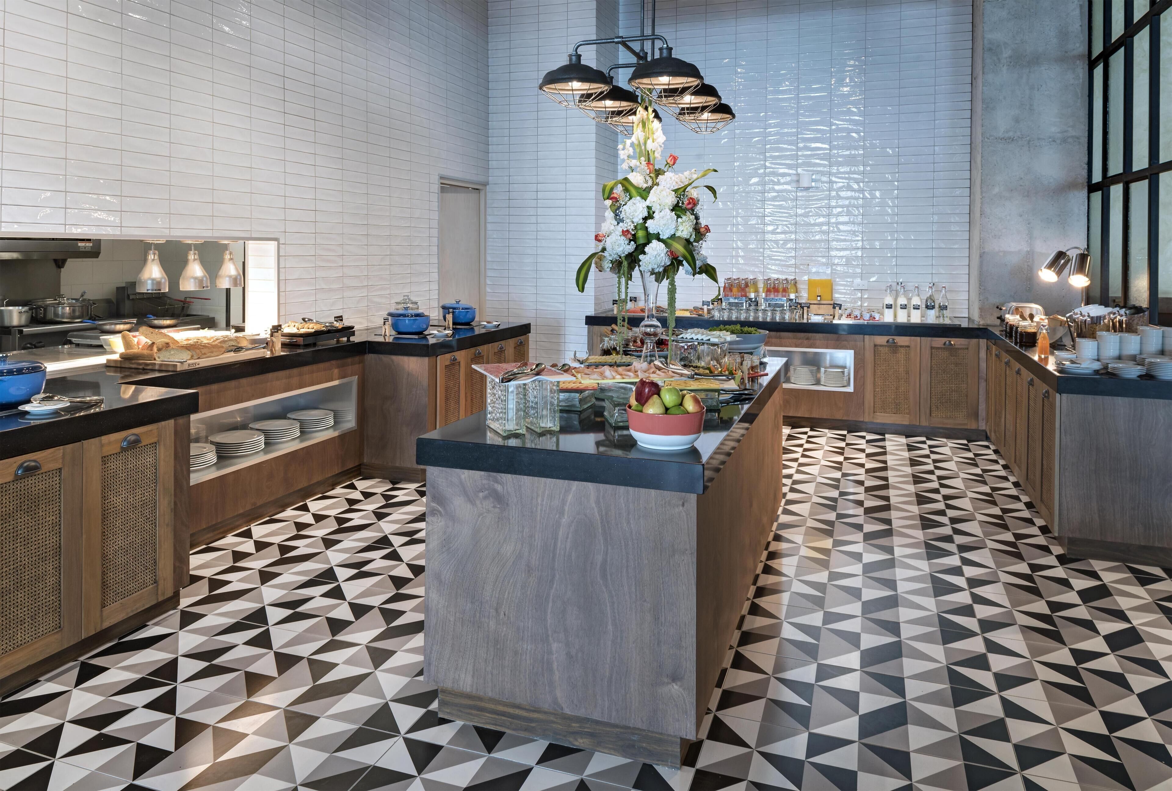 Una cocina moderna con piso de diseño geométrico, una isla central con un florero y un bufé con diversos alimentos y bebidas.