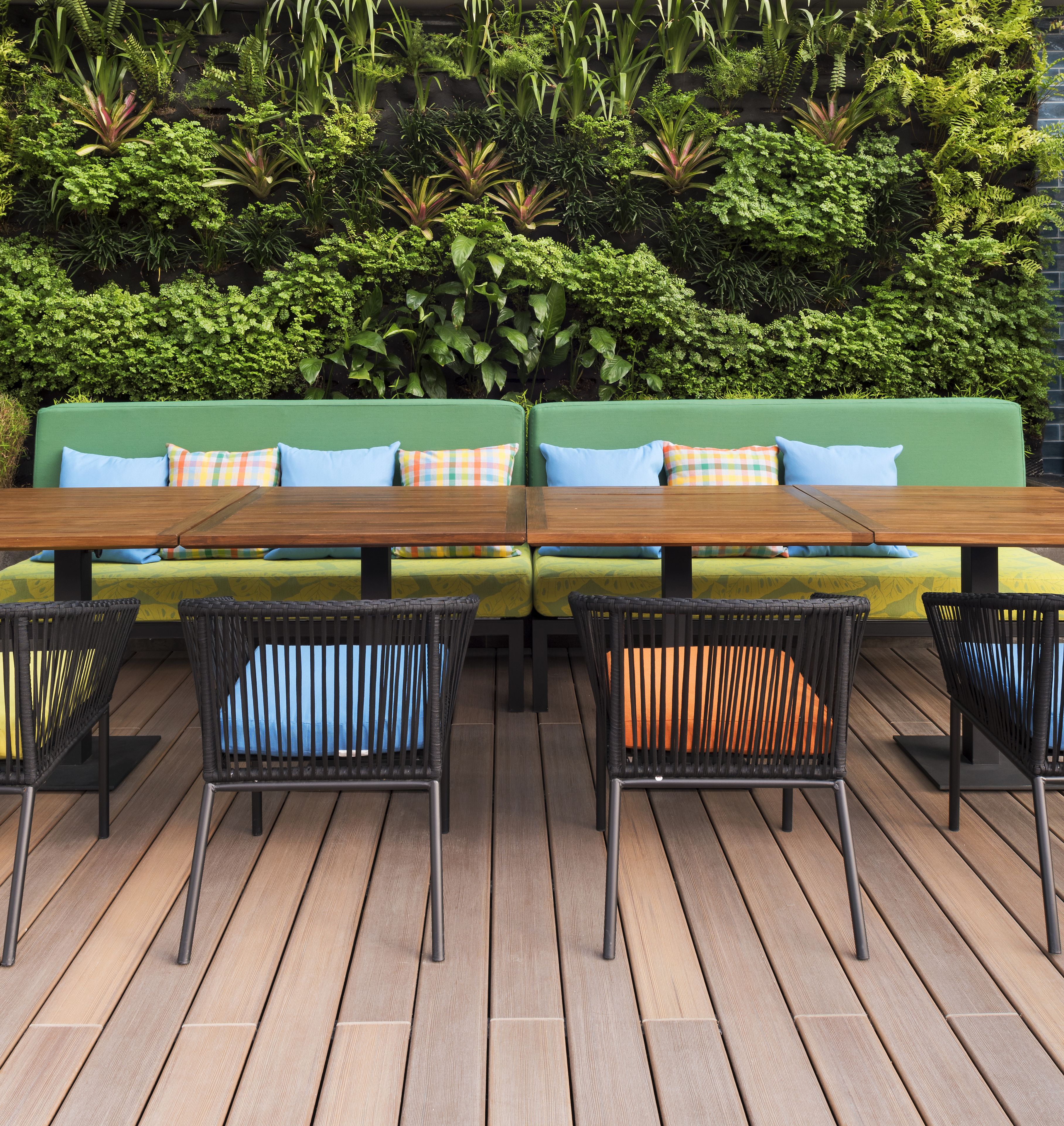 Una terraza de madera con un sofá verde y sillas de ratán negro.