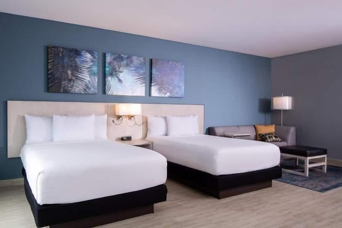 Ein Hotelzimmer mit zwei Betten, einem Schreibtisch, einem Stuhl und Bildern an der Wand.