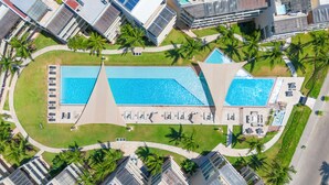 An aerial view of a hotel with two large swimming pools, surrounded by palm trees and a well-maintained lawn. - Castillo de Arena by NAS (Playa del Carmen)