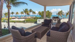 A covered outdoor seating area with wicker furniture, a grill, and a view of the beach and ocean. - Castillo de Arena by NAS (Playa del Carmen)
