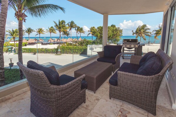 Un espace extérieur aménagé, abrité et doté de mobilier en osier, d’un barbecue et offrant une vue sur la plage et l’océan.